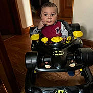 Koda joined the competition — help win amazing prizes! baby, batman, child, clothing, curious, expression, face, floor, footwear, furniture, hand, home, indoor, looking, person, sitting, toy, walker, wooden_floor, young_child
