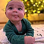 Koda is registered to the contest to win money with this photo: baby, blanket, bokeh, child, cozy, curious, cute, expression, eyes, face, green_clothing, hands, head, indoor, infant, lying_down, mouth, portrait, skin, warm_lighting