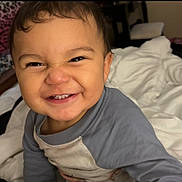 Koda is registered to the contest to win money with this photo: toddler, smiling, face, child, happy, indoor, bed, blanket, clothing, person, cute, portrait, young_child, expression, cozy, hair, skin, eyes, mouth, sitting