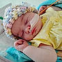 baby, sleeping, hat, yellow_clothing, blanket, nasal_tube, medical_tape, infant, cute, resting, soft_texture, pastel_colors, child, face, hand, indoors, peaceful, closeup, person, newborn