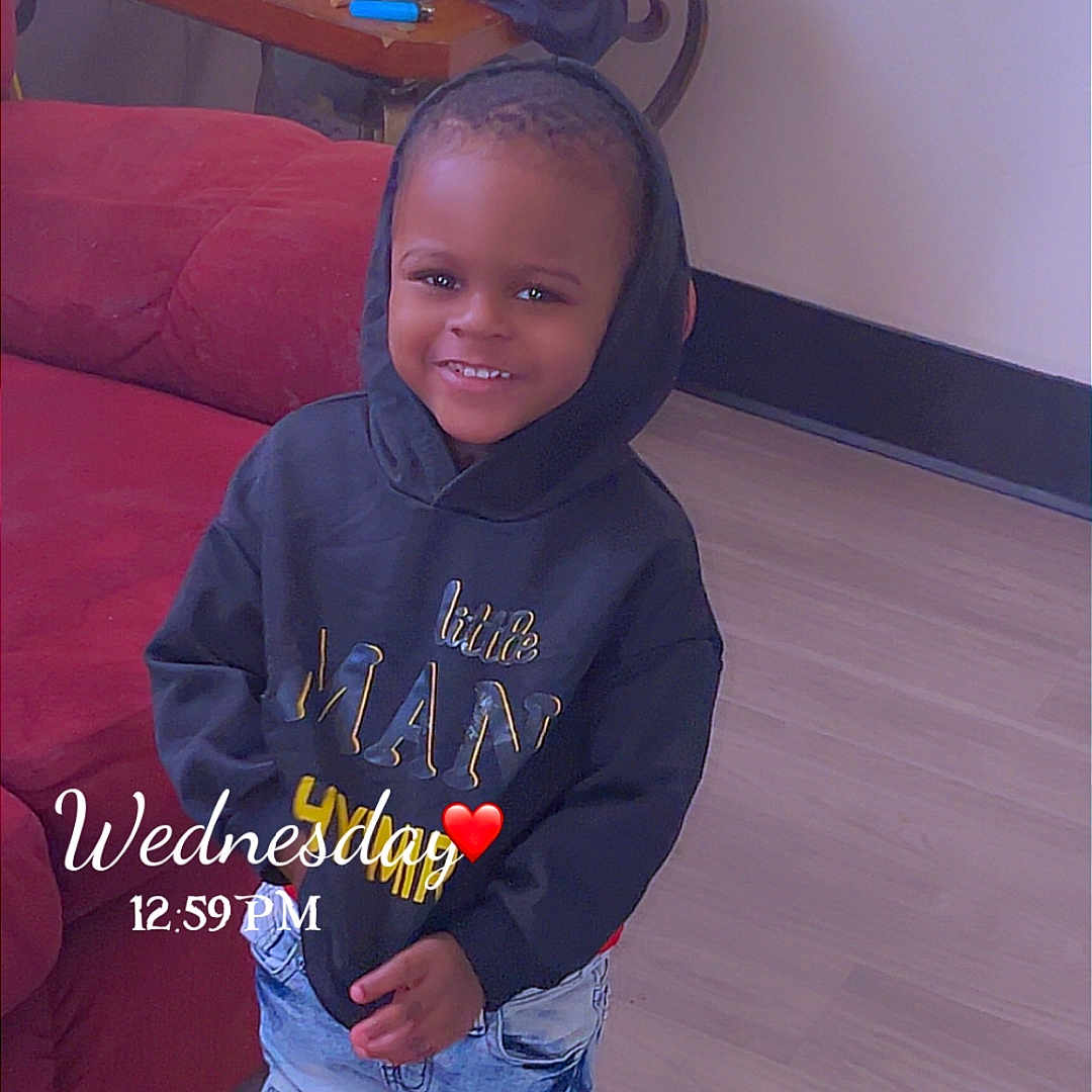 Hymir is registered to the contest to win money with this photo: child, toddler, hoodie, jeans, sneakers, smile, indoor, floor, furniture, couch, table, clutter, plastic_bag, toy, person, portrait, happy, casual, timestamp, overlay_text