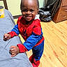 Hymir is registered to the contest to win money with this photo: child, toddler, costume, spiderman, smile, indoor, wood_floor, couch, can, plastic_bag, cabinet, happy, person, clothing, toy, home, floor, furniture, standing, portrait