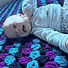 Penelope is registered to the contest to win money with this photo: baby, infant, crocheted_blanket, colorful, purple, blue, black, floral_clothing, long_sleeve, lying_down, playful, tongue_out, happy, indoors, soft_texture, cozy, cute, child, smiling, blanket