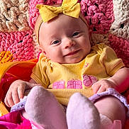 Penelope is registered to the contest to win money with this photo: baby, infant, smiling, yellow_bow, yellow_clothing, pink_socks, colorful_blanket, textured_blanket, happy, cute, portrait, child, face, headband, soft_toys, cozy, indoors, playful, closeup, person