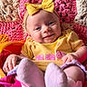 baby, infant, smiling, yellow_bow, yellow_clothing, pink_socks, colorful_blanket, textured_blanket, happy, cute, portrait, child, face, headband, soft_toys, cozy, indoors, playful, closeup, person