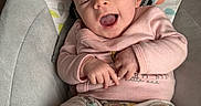 Penelope is registered to the contest to win money with this photo: baby, baby_chair, child, comfort, cozy, cushion, cute, face, hands, happy, headrest, indoor, infant, pajamas, patterned_fabric, person, pink_sweater, relaxing, smile, yawn