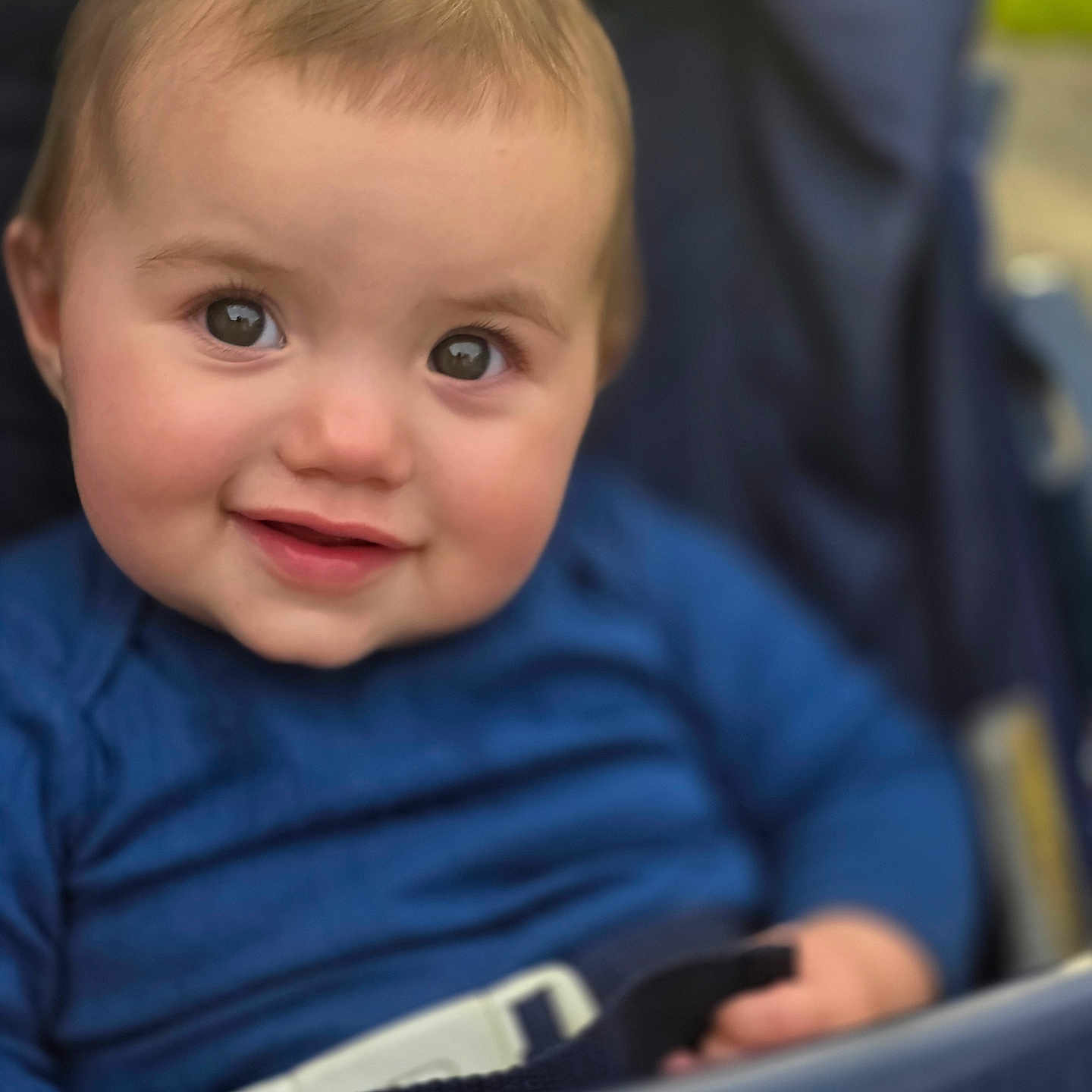 Willow is registered to the contest to win money with this photo: baby, child, smile, face, blue_clothing, stroller, seatbelt, cute, portrait, infant, happy, young_child, person, closeup, human, outdoor, daylight, expression, skin, head
