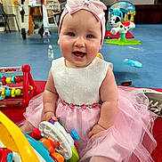 Rosie is registered to the contest to win money with this photo: baby, child, smiling, dress, headband, toy, indoor, floor, sitting, cute, play, pink, white, happy, infant, girl, colorful, mat, fun, portrait