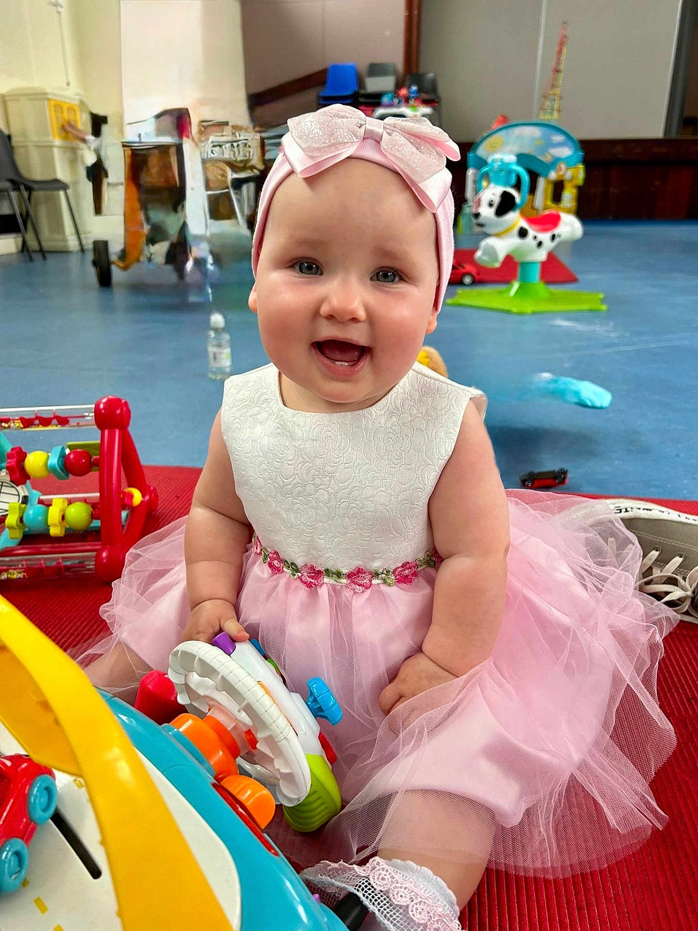 Rosie is registered to the contest to win money with this photo: baby, child, smiling, dress, headband, toy, indoor, floor, sitting, cute, play, pink, white, happy, infant, girl, colorful, mat, fun, portrait