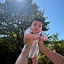 baby, infant, arms, tattoos, sunlight, tree, outdoor, child, person, sky, nature, daylight, holding, cute, portrait, people, casual, summer, young, background