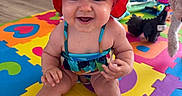 Scarlet is registered to the contest to win money with this photo: baby, child, smiling, hat, swimsuit, colorful, playmat, toy, floor, indoor, happy, person, cute, infant, sitting, headwear, bright, home, pet, fun