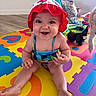 baby, child, smiling, hat, swimsuit, colorful, playmat, toy, floor, indoor, happy, person, cute, infant, sitting, headwear, bright, home, pet, fun