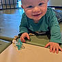 baby, smiling, blue_eyes, crawling, pacifier, toy, beads, mat, indoor, child, play_area, furniture, storage, person, happy, clothing, head, hand, floor, portrait
