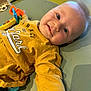 baby, infant, smiling, yellow_shirt, toy, indoor, child, cute, playful, lying_down, pacifier, face, closeup, happy, young_child, casual_clothing, soft_surface, blue_eyes, light_hair, baby_toys