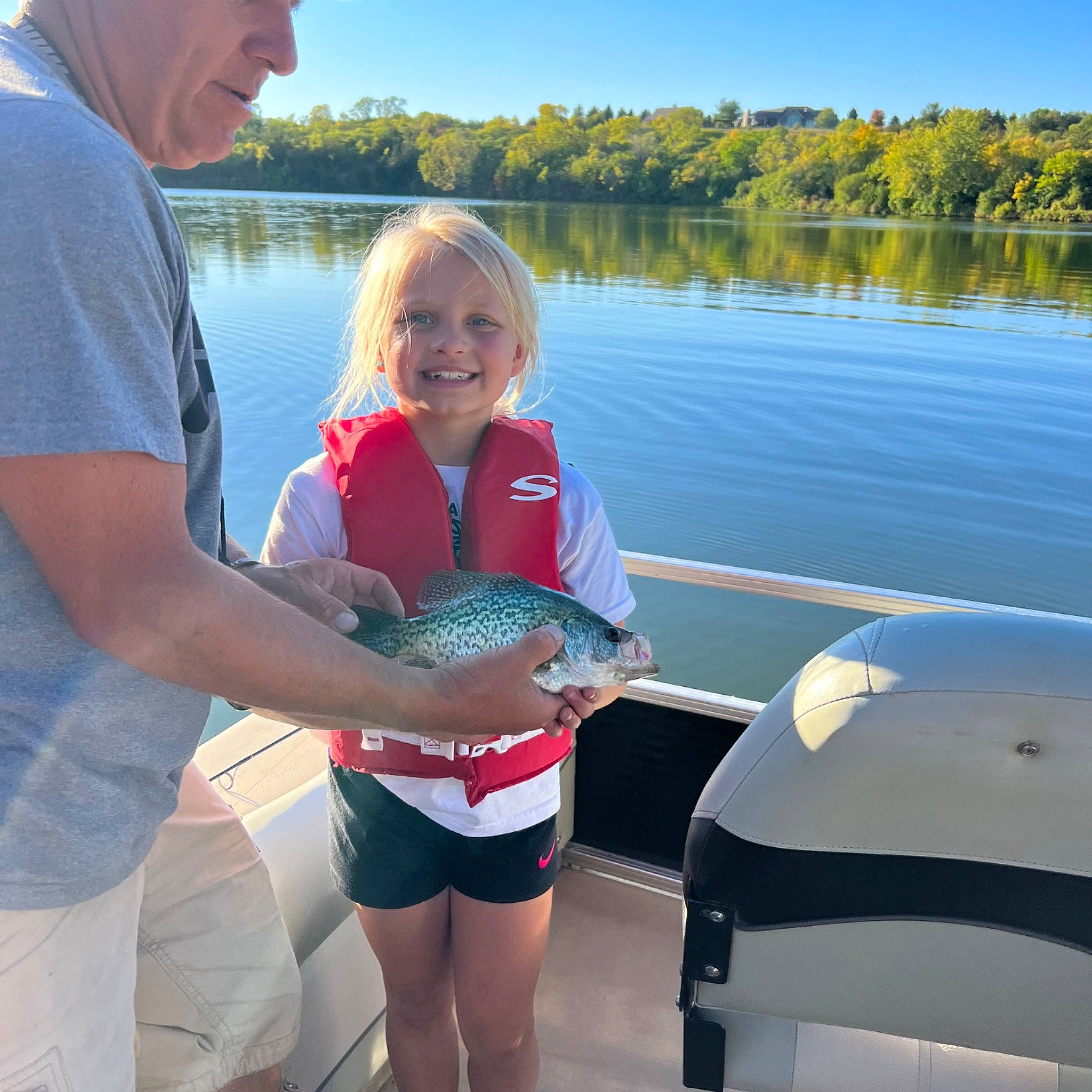 Karsyn is registered to the contest to win money with this photo: baseball_cap, blue, body_of_water, cap, eyewear, fun, glasses, hat, joy, lake, leisure, person, shorts, sky, smile, summer, t_shirt, thigh, travel, tree