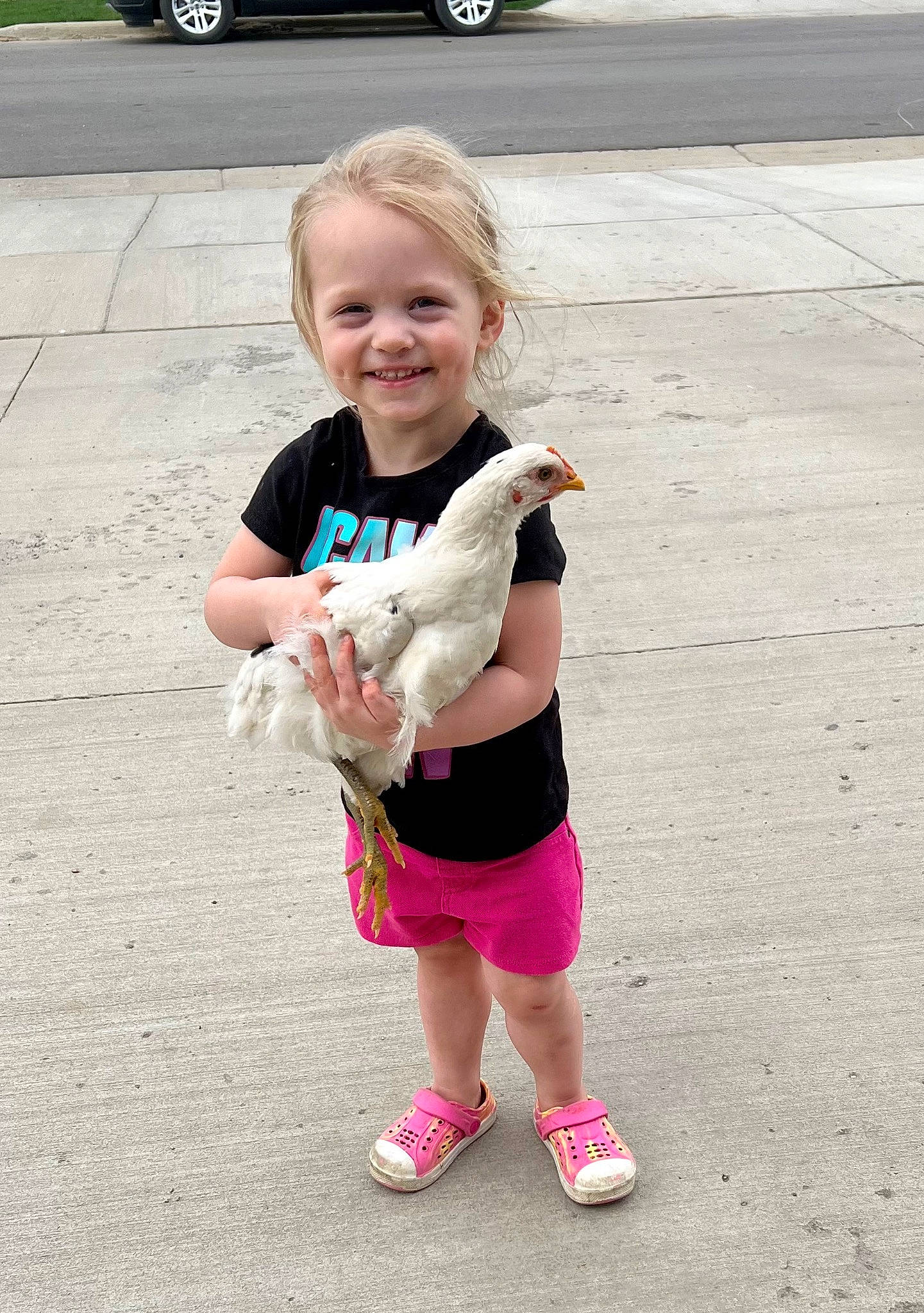 Jensyn is registered to the contest to win money with this photo: asphalt, car, eyewear, face, footwear, grass, hand, happy, human_leg, joy, knee, leisure, person, pink, recreation, shorts, sleeve, smile, sneakers, t_shirt