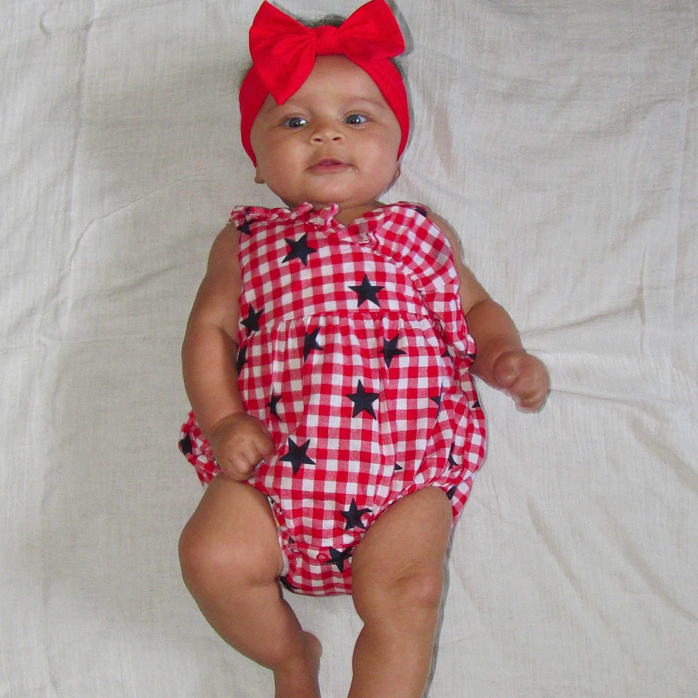Aurora is registered to the contest to win money with this photo: arms, baby, bow, checkered_pattern, child, cute, eyes, fabric_background, head, infant, legs, lying_down, mouth, person, photography, red_headband, red_outfit, skin, smiling, stars
