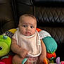 Aurora is registered to the contest to win money with this photo: baby, child, infant, plush_toy, colorful, bib, couch, black_leather, patterned, pink, green, orange, purple, cute, sitting, indoor, portrait, soft_toy, curious, pout