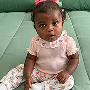 Zuri is registered to the contest to win money with this photo: baby, child, girl, pink_bows, curly_hair, green_background, sitting, cute, strawberry_pattern, white_socks, curious, portrait, indoors, clothing, infant, expression, closeup, person, young_child, adorable
