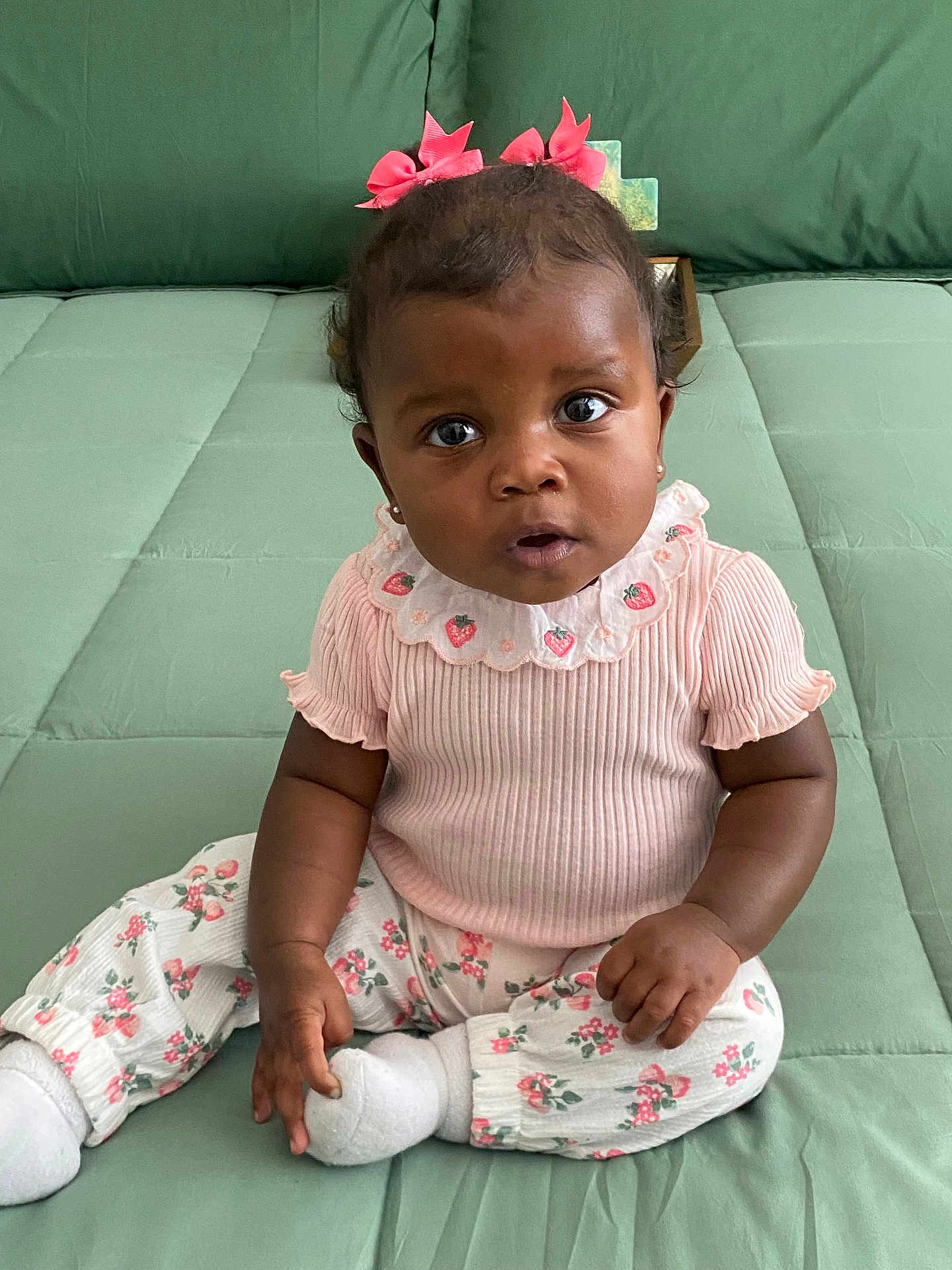 Zuri is registered to the contest to win money with this photo: baby, child, girl, pink_bows, curly_hair, green_background, sitting, cute, strawberry_pattern, white_socks, curious, portrait, indoors, clothing, infant, expression, closeup, person, young_child, adorable