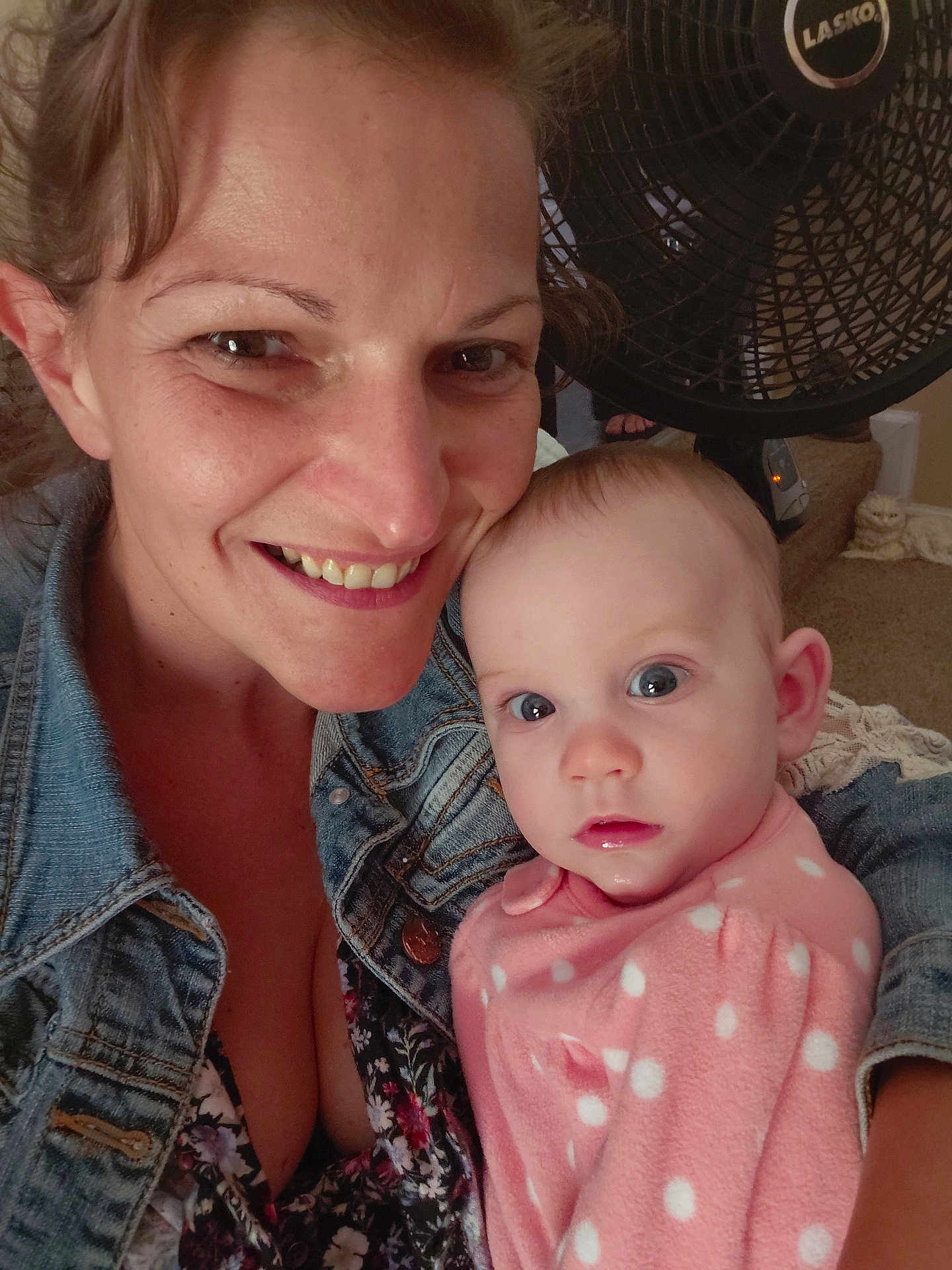 Hope is registered to the contest to win money with this photo: woman, baby, denim_jacket, pink_clothing, polka_dot, face, smile, indoor, fan, carpet, person, child, holding, portrait, closeup, happy, casual, home, light, expression
