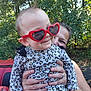adult, baby, casual, child, cute, fashion, fun, hands, happy, heart_shaped_glasses, holding, leopard_print, nature, outdoor, person, portrait, red_sunglasses, smile, sunlight, trees