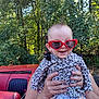 baby, car, child, clothing, cute, fashion, hands, happy, headwear, heart_shaped, leopard_print, nature, outdoor, person, portrait, red, smiling, sunglasses, sunlight, trees