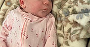 Elliana is registered to the contest to win money with this photo: baby, blanket, cherry_pattern, child, cozy, cute, expression, face, floral_blanket, head, indoors, infant, lying_down, pink_onesie, pout, skin, sleepwear, soft_texture, warm, young