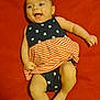 Zahara is registered to the contest to win money with this photo: baby, smiling, infant, dress, stars, stripes, red_blanket, happy, child, cute, laying_down, skin, foot, hand, cheerful, clothing, face, portrait, one_person, indoors