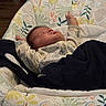 baby, sleeping, infant, blanket, baby_seat, cushion, patterned_fabric, indoor, peaceful, arms_stretched, clothing, newborn, head, face, resting, comfort, cute, child, portrait, soft_lighting