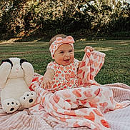Ivory is registered to the contest to win money with this photo: baby, blanket, child, cute, dog_toy, floral_clothing, grass, happy, headband, heart_pattern, nature, outdoor, pink, playful, plush_toy, portrait, sitting, smiling, sunlight, toy