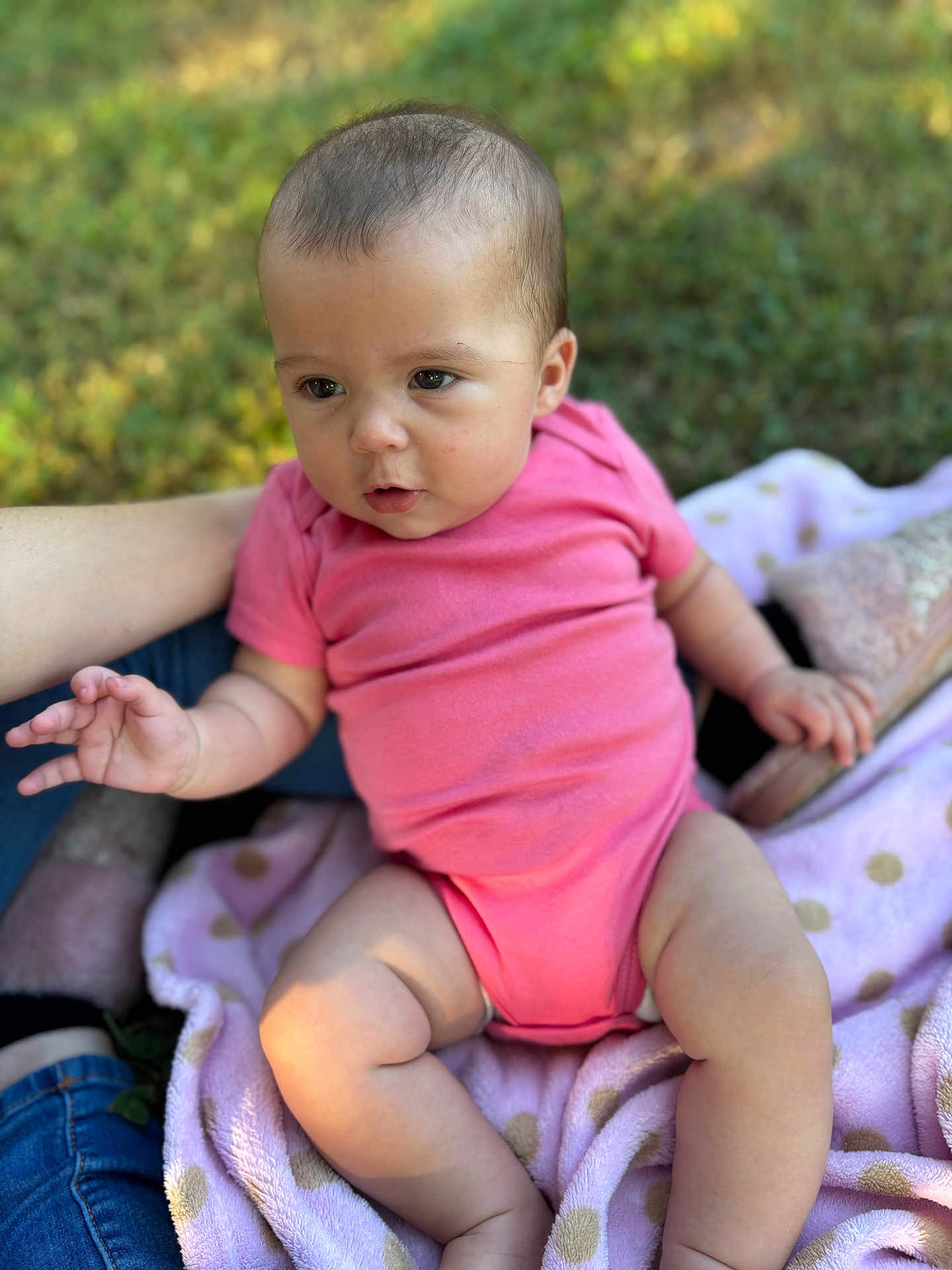 Ivory is registered to the contest to win money with this photo: baby, infant, pink_onesie, blanket, polka_dots, outdoor, grass, person, skin, legs, arm, hand, footwear, nature, casual_clothing, sitting, supporting_arm, soft_texture, closeup, daylight