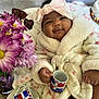 baby, child, smiling, robe, headband, bow, mug, flowers, purple_flowers, cake, table, indoor, soft_texture, cute, portrait, happy, infant, warm_clothing, decor, celebration