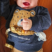 Lío participe au concours pour gagner de l'argent avec cette photo : baby, bear_design, blanket, brown_pants, child, closeup, clothing, cute, expression, happy, indoors, infant, lying_down, pacifier, playful, portrait, raised_fists, smiling, sweater, young