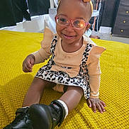Kay'Cee is registered to the contest to win money with this photo: toddler, child, smiling, glasses, headband, bow, dress, leopard_print, boots, sitting, yellow_blanket, indoor, happy, person, furniture, fan, curtains, floor, hand, footwear