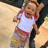 Naziyah is registered to the contest to win money with this photo: baby, child, smiling, standing, adult_hands, headband, colorful_pants, sneakers, outdoor, concrete, car_door, person, footwear, happy, cute, walking, support, casual_clothing, daylight, playful