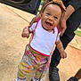 baby, child, smiling, standing, adult_hands, headband, colorful_pants, sneakers, outdoor, concrete, car_door, person, footwear, happy, cute, walking, support, casual_clothing, daylight, playful