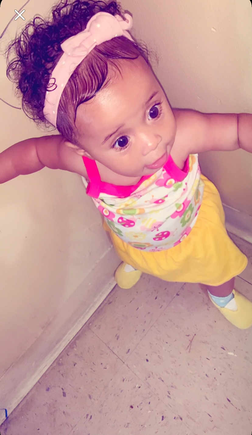 Naziyah is registered to the contest to win money with this photo: child, toddler, headband, curly_hair, pink_headband, colorful_clothing, yellow_skirt, floral_top, indoors, floor, wall, standing, big_eyes, cute, person, baby, socks, yellow_slippers, expression, portrait