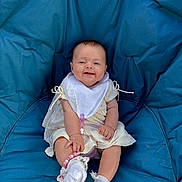 Poppy joined the competition — help win amazing prizes! baby, child, smiling, blue_cushion, bib, white_clothing, socks, lace, pacifier_clip, seated, indoor, cute, happy, infant, portrait, person, young_child, comfortable, casual, baby_accessory