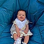 baby, child, smiling, blue_cushion, bib, white_clothing, socks, lace, pacifier_clip, seated, indoor, cute, happy, infant, portrait, person, young_child, comfortable, casual, baby_accessory