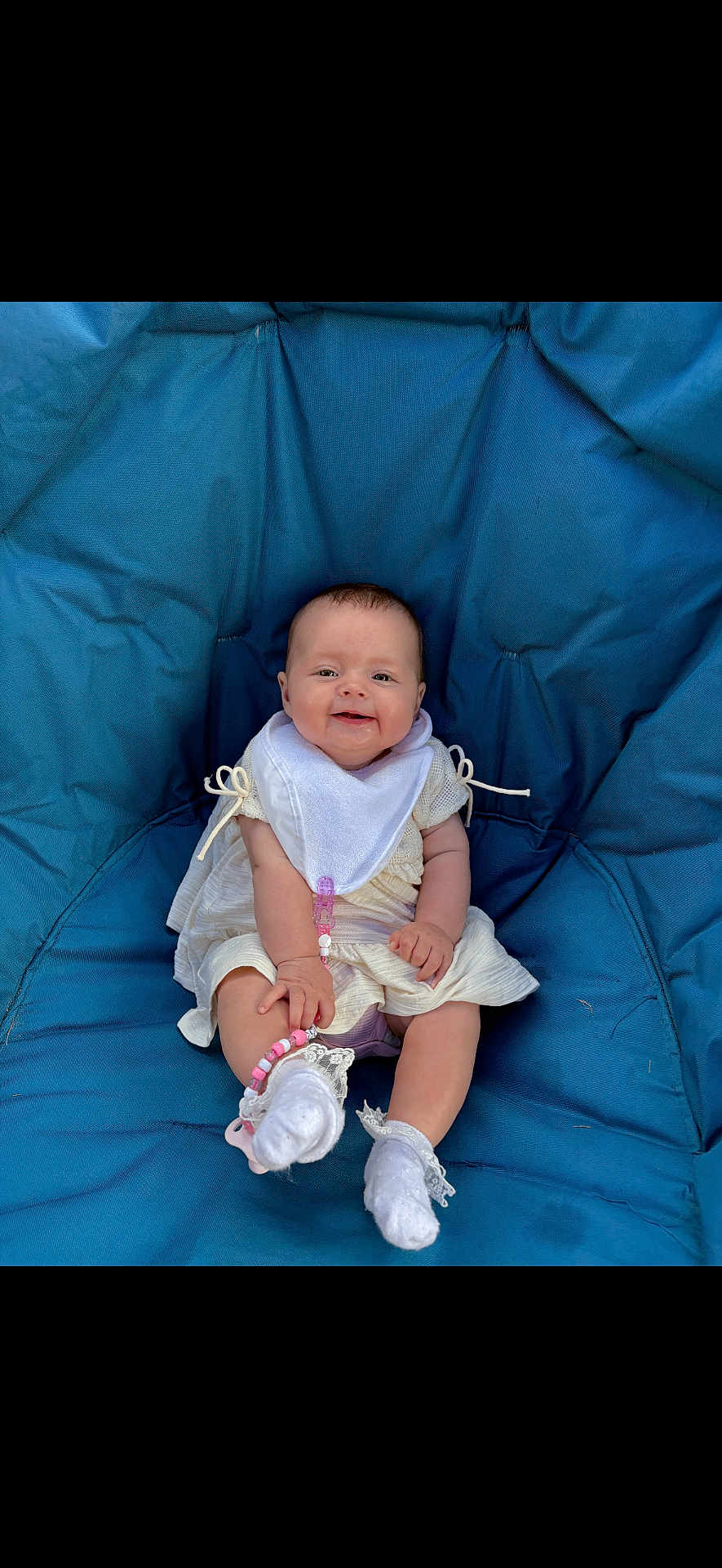 Poppy joined the competition — help win amazing prizes! baby, child, smiling, blue_cushion, bib, white_clothing, socks, lace, pacifier_clip, seated, indoor, cute, happy, infant, portrait, person, young_child, comfortable, casual, baby_accessory