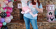 Ava is registered to the contest to win money with this photo: woman, child, balloons, birthday_party, mouse_ears, pink, blue, stone_fireplace, decorative_blocks, celebration, indoor, casual_clothing, jeans, toddler, smile, holding, party_decor, floor, cheerful, family
