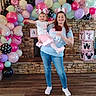 woman, child, balloons, birthday_party, mouse_ears, pink, blue, stone_fireplace, decorative_blocks, celebration, indoor, casual_clothing, jeans, toddler, smile, holding, party_decor, floor, cheerful, family