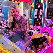 Sushi participe au concours pour gagner de l'argent avec cette photo : woman, dog, kiddie_ride, furry_coat, blonde_hair, pink_car, yellow_car, indoor, neon_sign, colorful, carnival, amusement_ride, pet, smiling, casual, playful, fun, decorations, night, lights