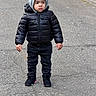 black_jacket, casual_clothing, child, cold_weather, fashion, footwear, hoodie, jacket, outdoor, pants, pavement, person, serious_expression, sidewalk, sneakers, standing, street, toddler, urban, young_child
