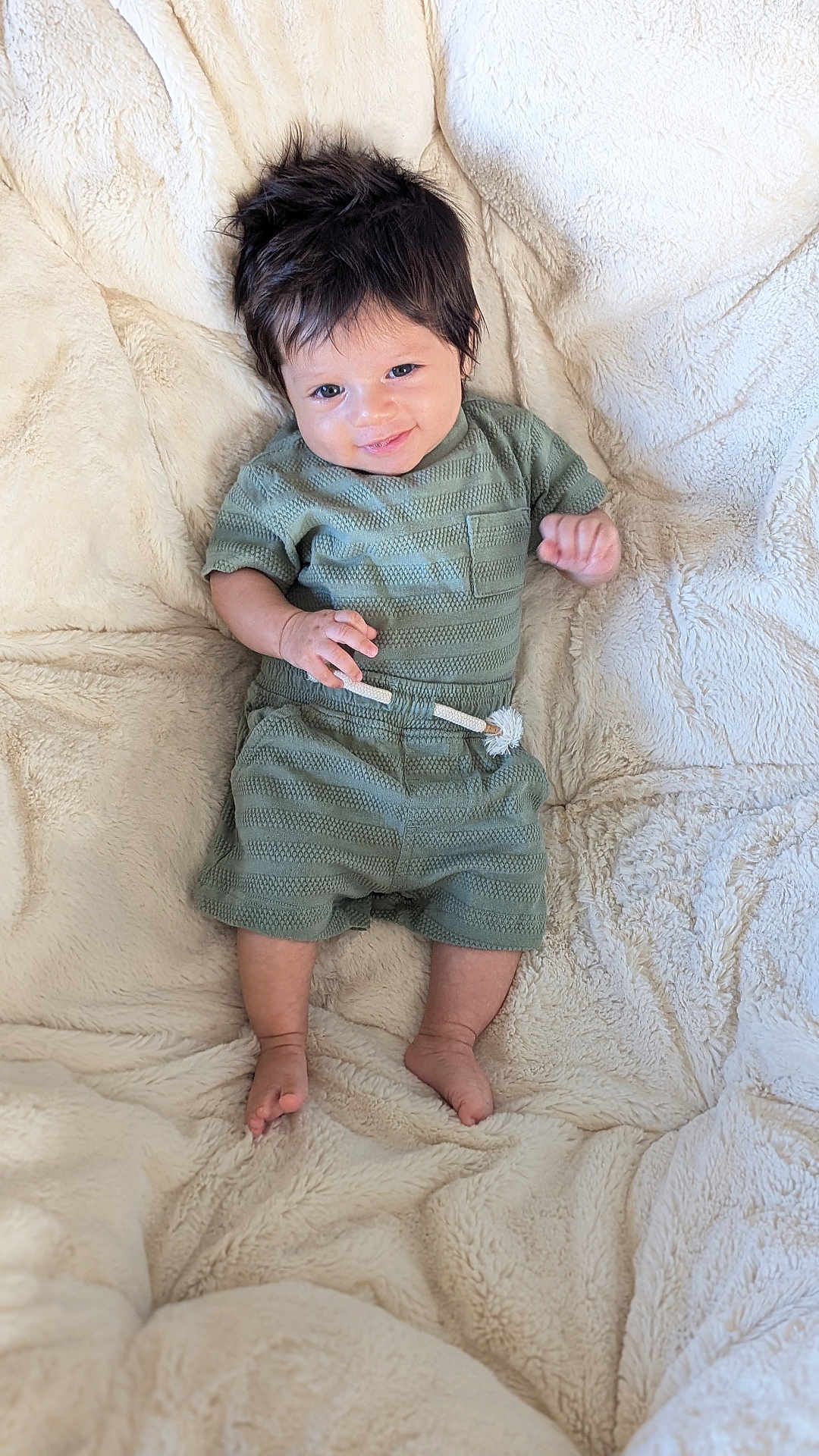 Azari is registered to the contest to win money with this photo: baby, child, infant, smile, happy, green_outfit, shorts, tshirt, dark_hair, barefoot, blanket, soft_texture, lying_down, cute, portrait, indoors, cozy, small_hands, small_feet, comfortable