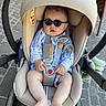 baby, sunglasses, car_seat, stroller, child, cobblestone, outdoor, feet, legs, hands, clothing, straps, safety, cute, sunny, head_support, toy, fashion, infant, relaxing