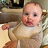 Léandre a rejoint le concours — aidez-le/la à gagner de superbes lots ! baby, child, high_chair, bib, messy_face, food, sweater, indoor, furniture, table, face, hand, curious, young_child, person, living_room, television, cozy, seat, cute