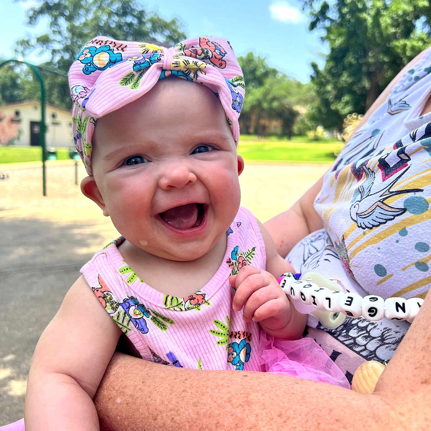 Angelique joined the competition — help win amazing prizes! baby, child, smile, laughing, pink_bow, pink_dress, outdoor, sunny, park, greenery, adult_arm, happy, headwear, person, clothing, daylight, nature, holding, toddler, portrait