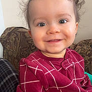 Oliver is registered to the contest to win money with this photo: baby, child, smiling, happy, face, hair, clothing, maroon, pattern, couch, indoor, portrait, seated, young_child, cute, person, expression, cozy, casual, background